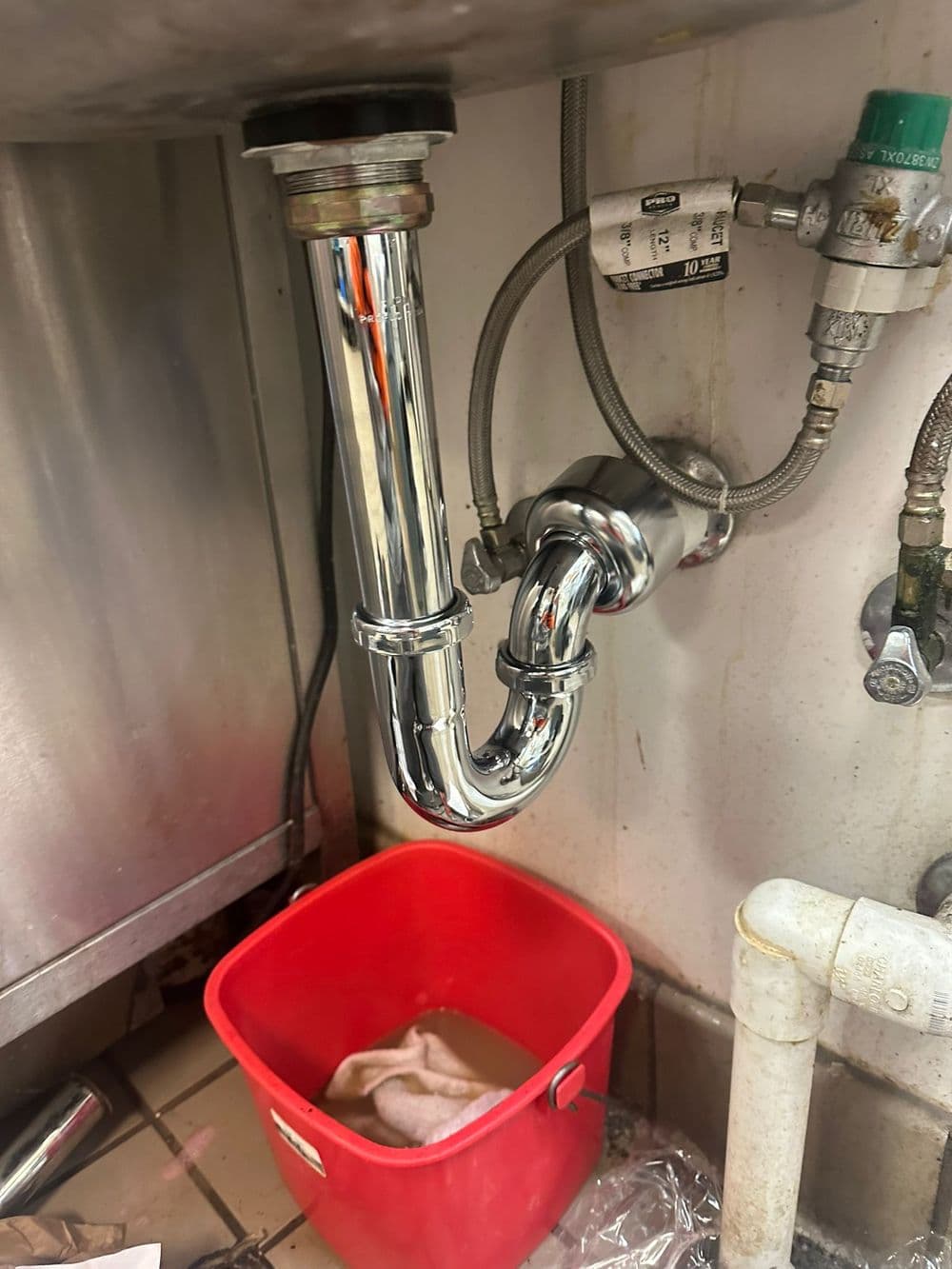 Chrome sink drain pipe with a red bucket underneath, capturing potential leaks.