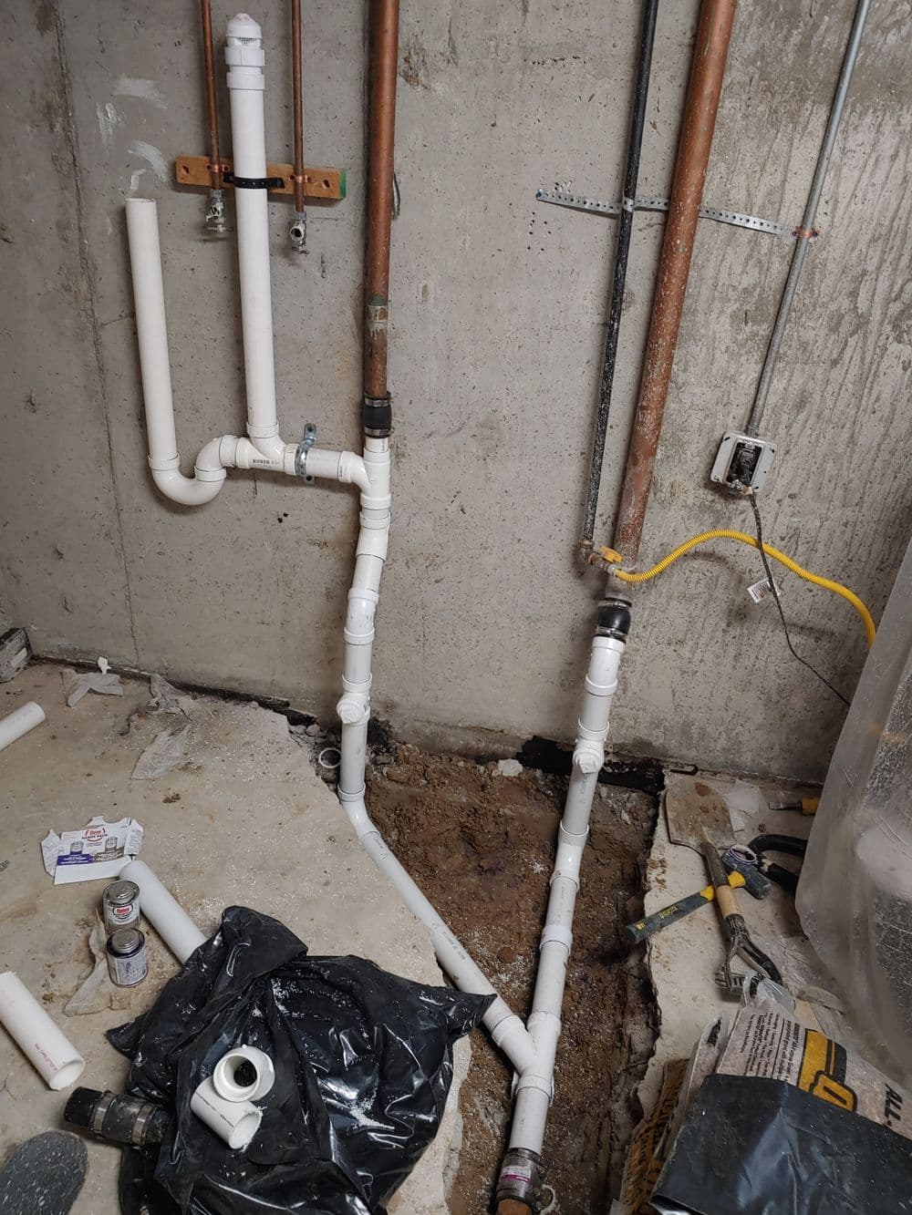 Newly installed plumbing pipes in a basement with exposed concrete walls and tools nearby.
