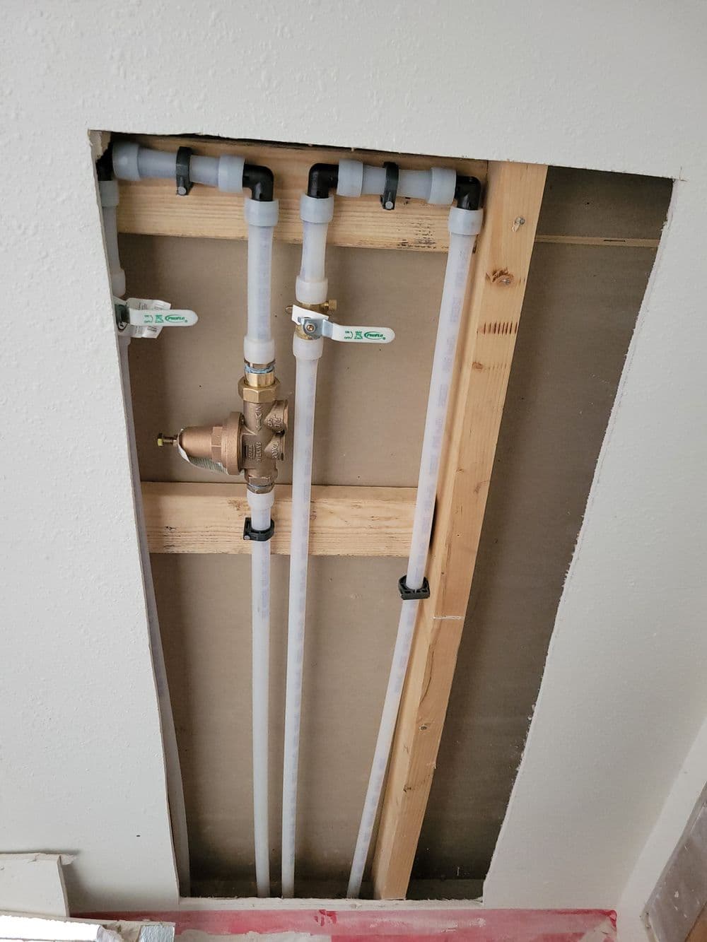 Exposed plumbing pipes and water valve installation in a home renovation project.