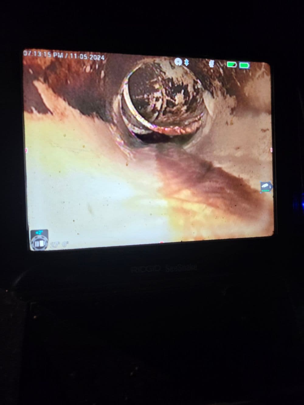 Camera view of a sewer inspection showing pipes and buildup inside a drainage system.