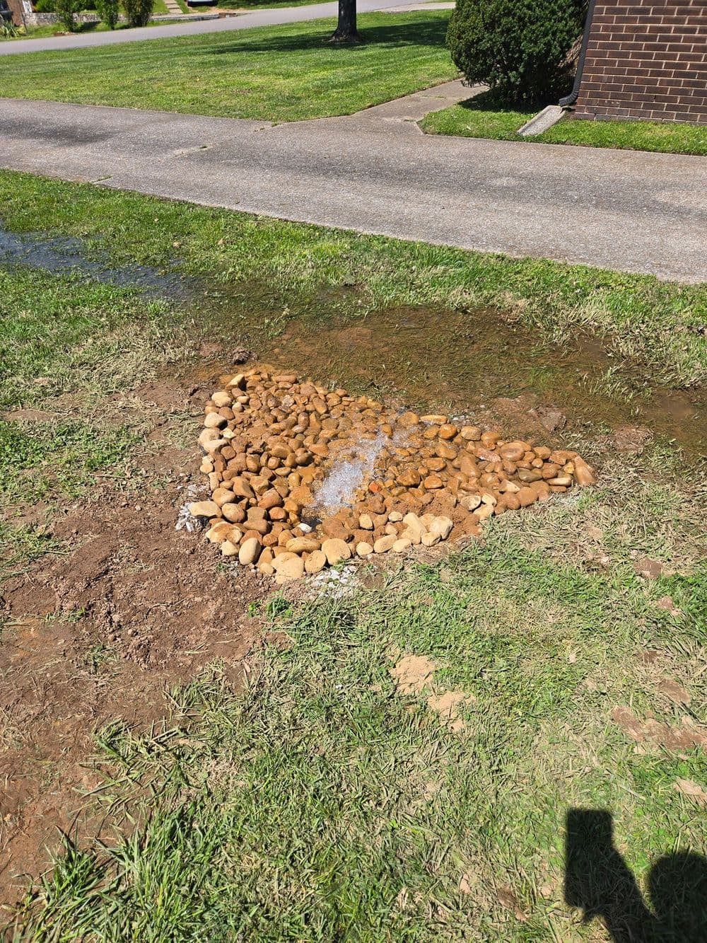 Stream of water flowing over a decorative rock formation in a grassy yard.