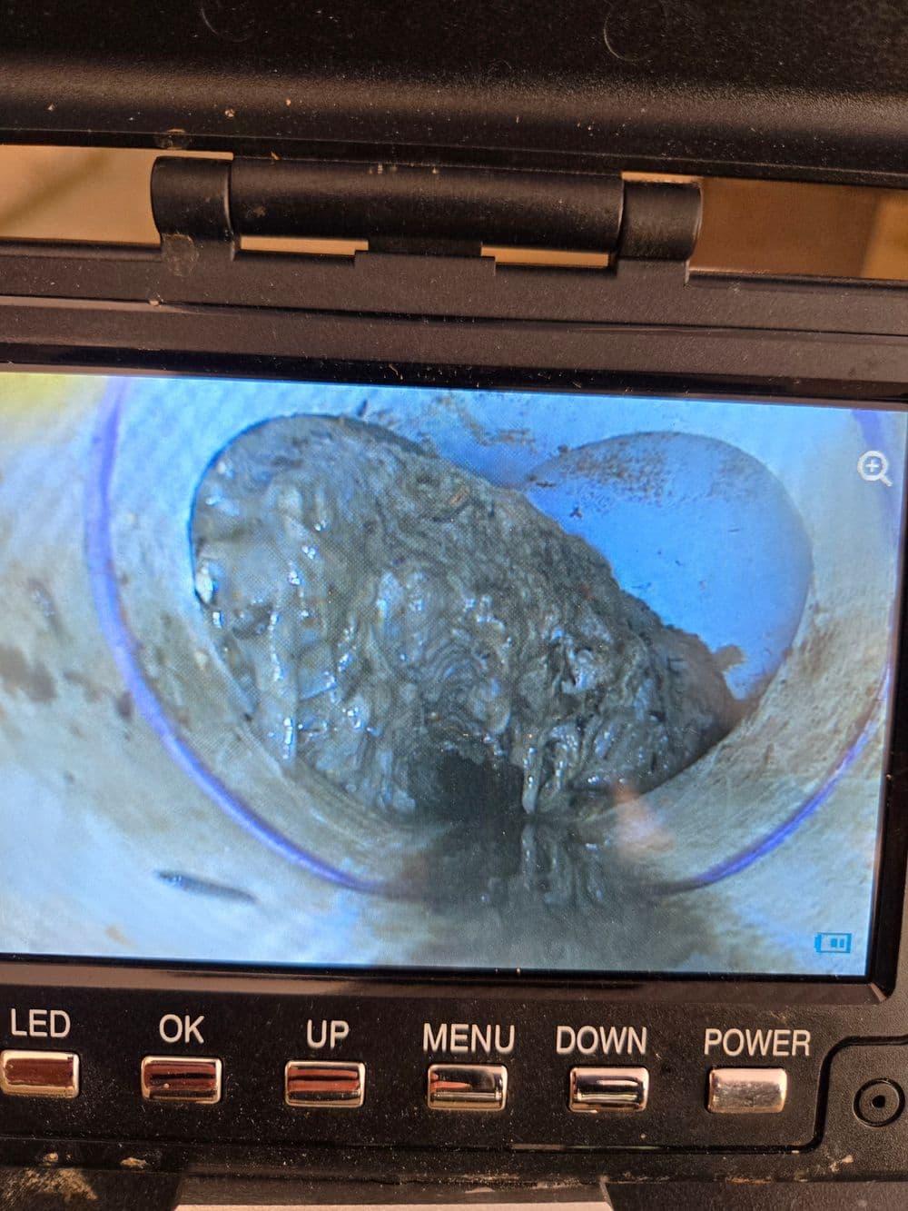 Camera view inside a clogged pipe showing thick buildup and blockage.